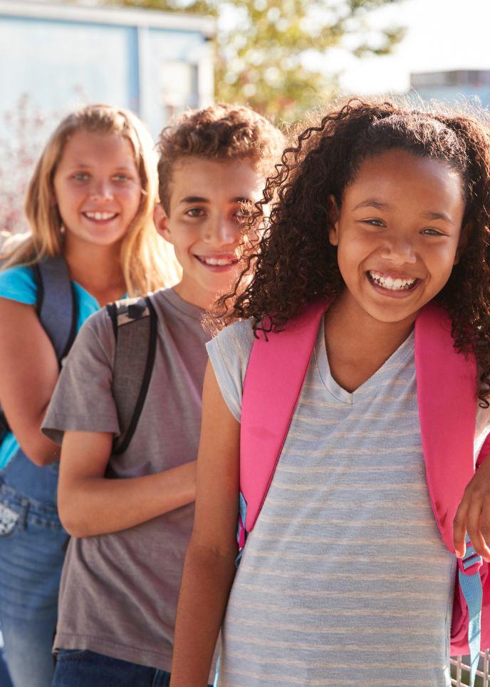 Kids wearing backpacks smiling at school